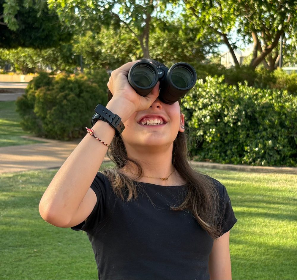 A young person in Laverton looks skyward through binoculars
